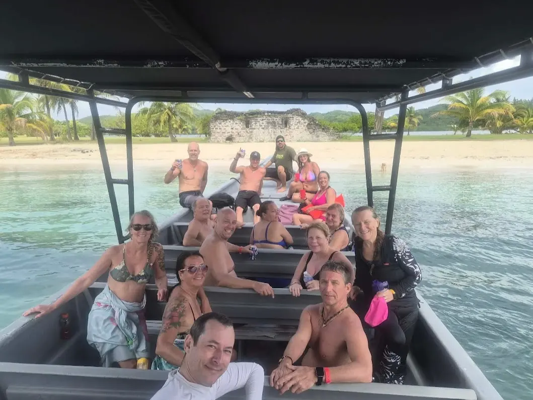 Groupe de voyageurs québécois à bord du bateau, devant une plage de sable blanc et les ruines d'un vieux fort