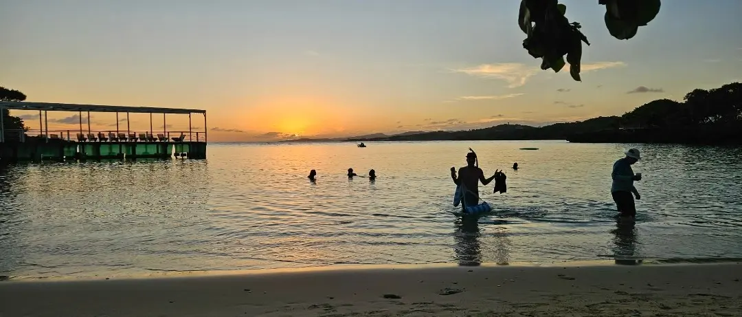 Baigneurs profitant du coucher de soleil dans les eaux calmes devant la plage