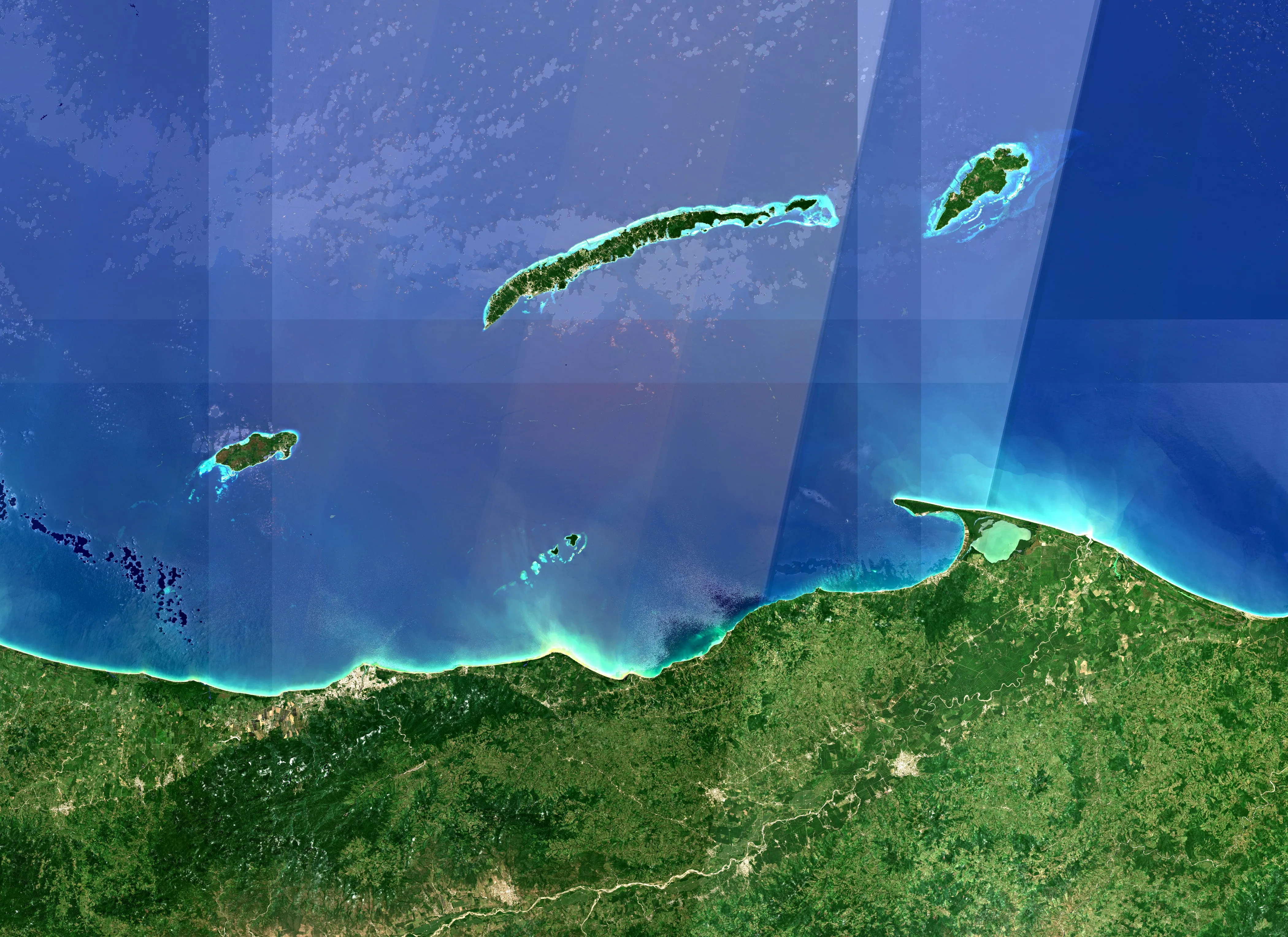 Les îles de la Baie du Honduras vues de l'espace : Útila à gauche, Roatán au centre avec son récif turquoise, Guanaja à droite, les Cayos Cochinos au sud et la côte de La Ceiba en bas.