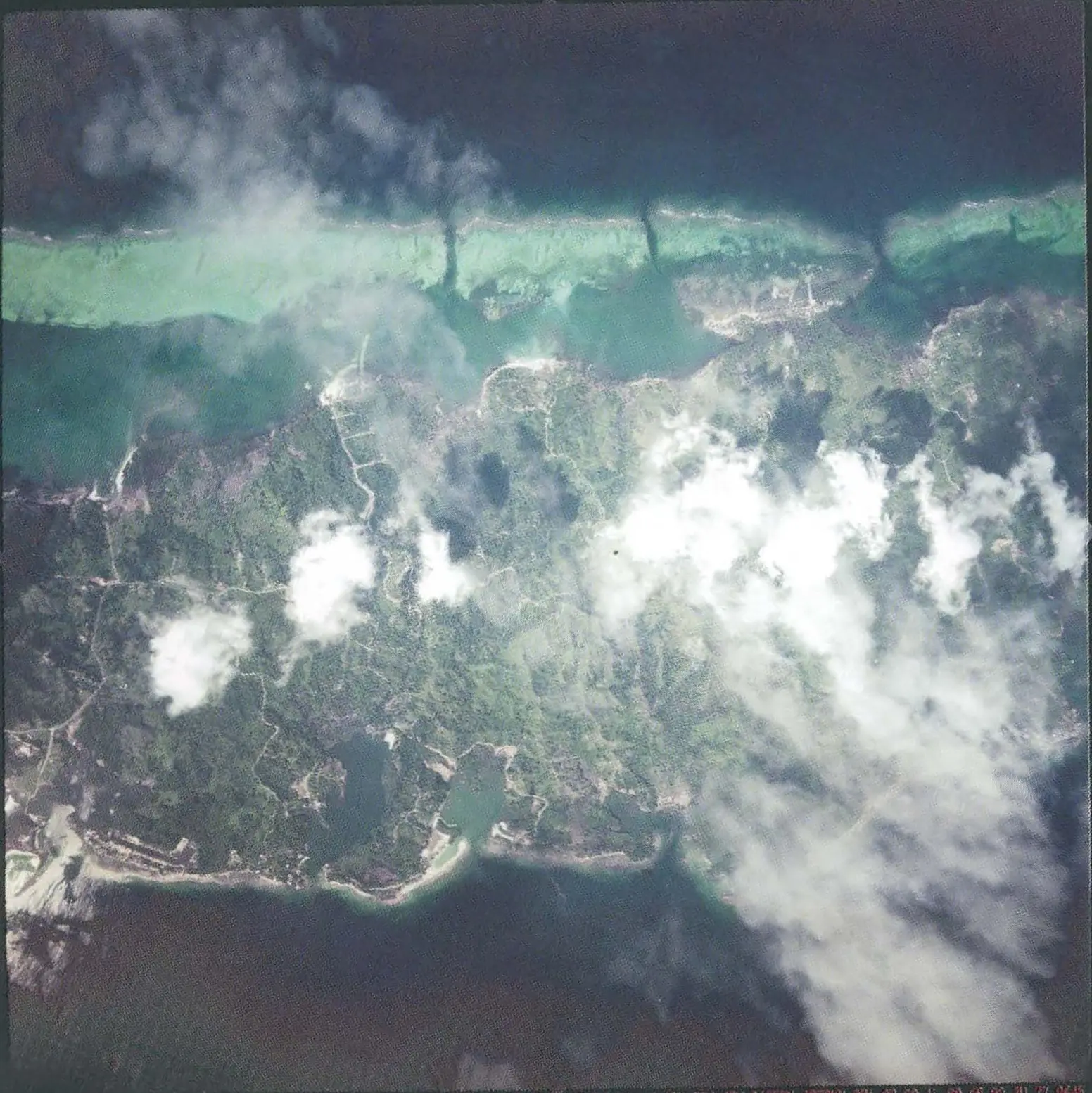 Photographie aérienne du centre de Roatán prise le 4 décembre 1998, cinq semaines après l’ouragan Mitch, montrant la ligne de récif et l’île verte