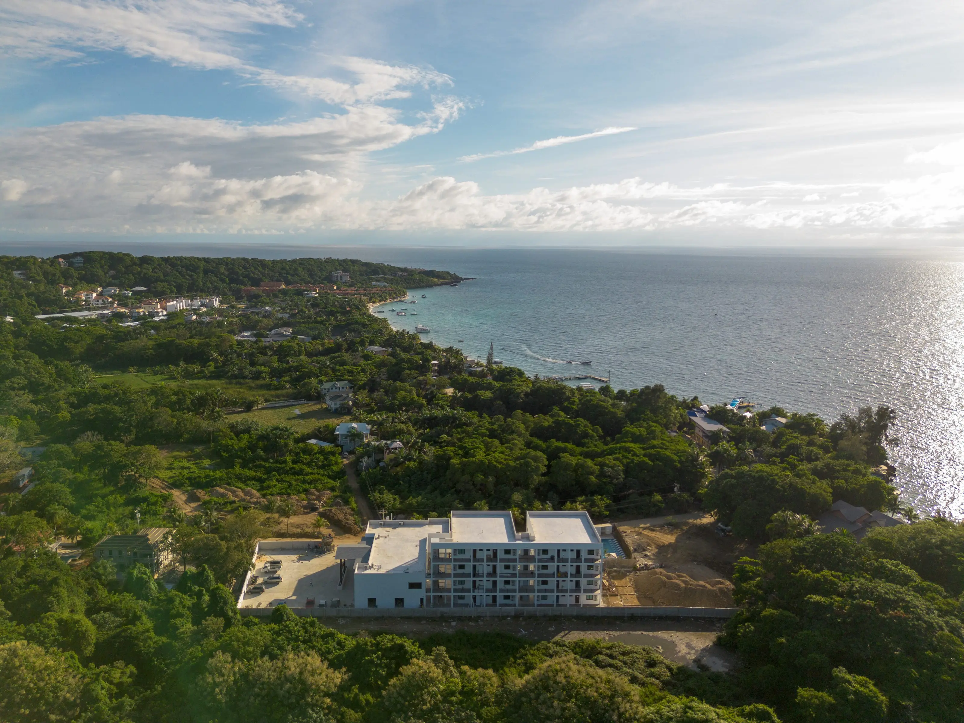 Aerial view of Acqua di Mare Roatán: the building set back in the greenery, with West Bay and its dock beyond