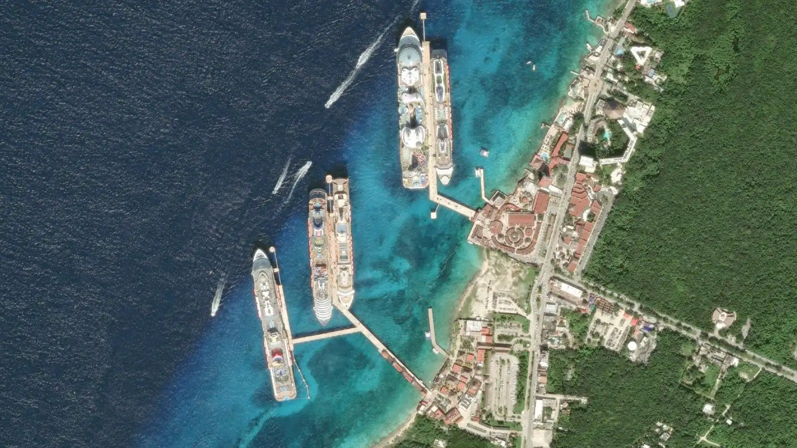 Cozumel cruise port seen from above: five cruise ships alongside the International Pier and Puerta Maya, the turquoise reef and San Miguel's coast road