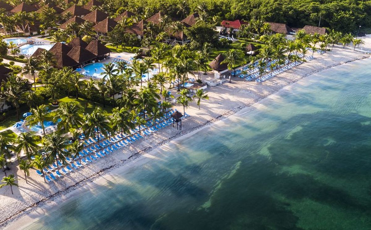 Vue aerienne d Allegro Cozumel : les toits de palme en pointe, les piscines et les rangees de chaises longues bleues le long du rivage.