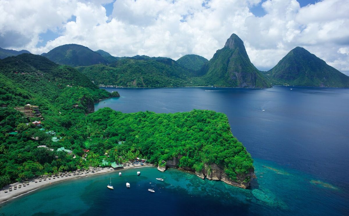 Vue aerienne de l'anse d'Anse Chastanet : la plage volcanique, le complexe dans la vegetation et les Pitons a l'arriere-plan.