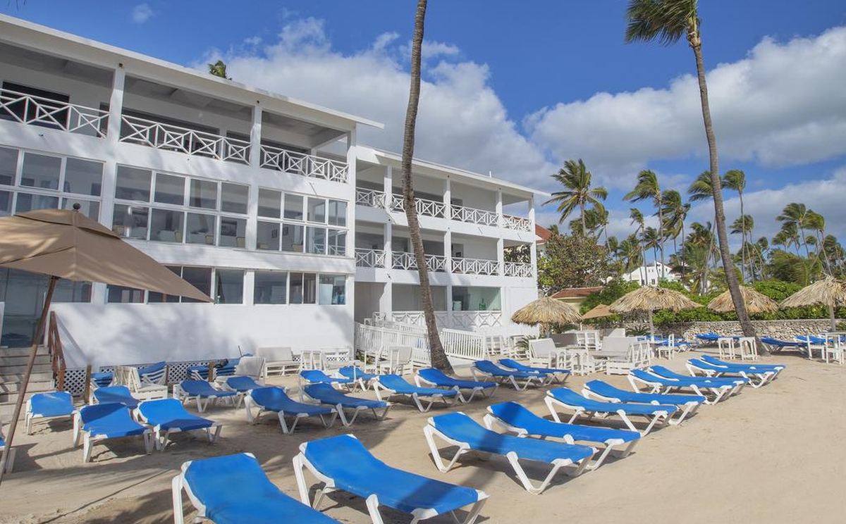 Le batiment blanc du Whala Bávaro vu depuis la plage, avec ses rangees de chaises longues bleues sur le sable.